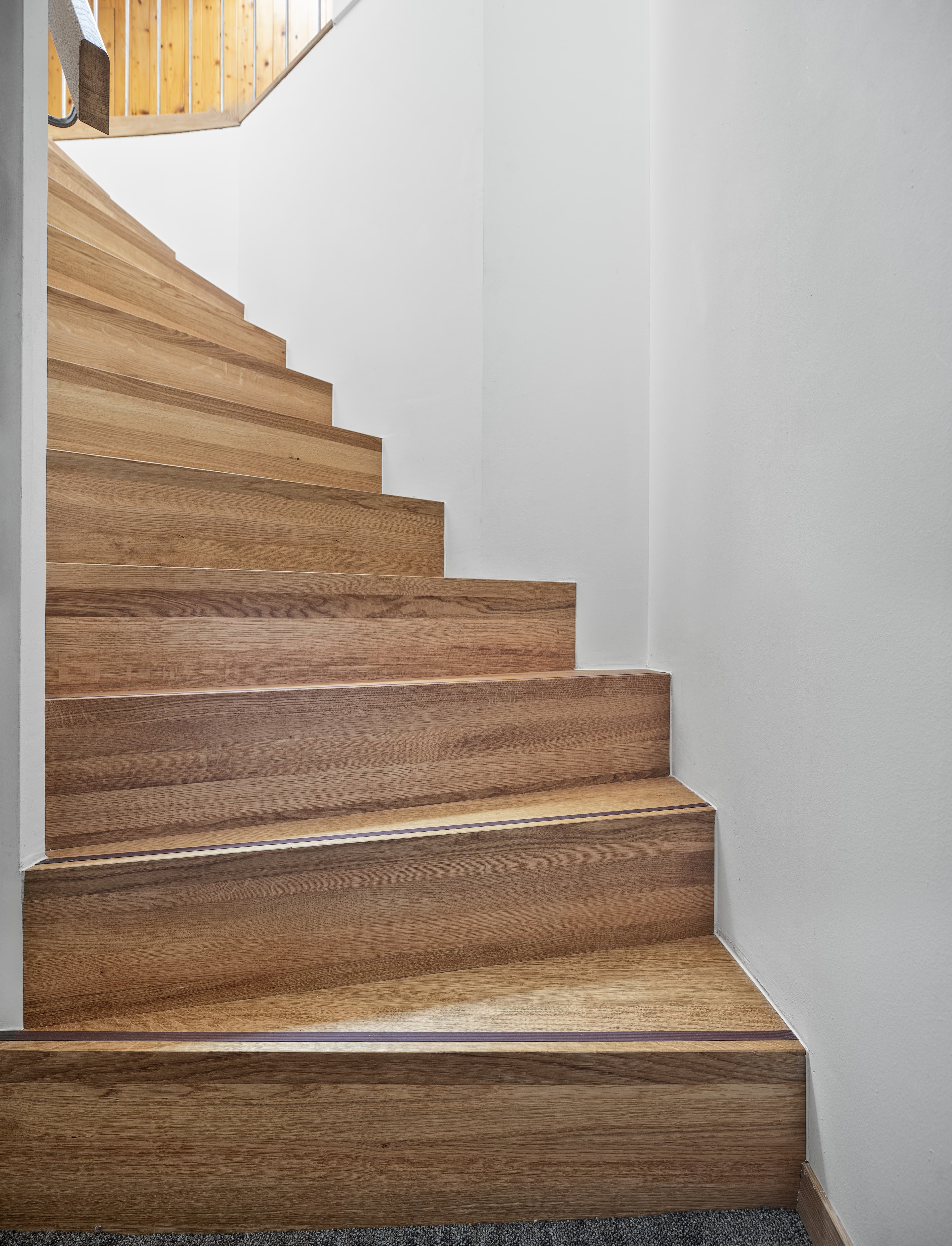 A wooden staircase in Hotel Krone by B Smart leads upwards surrounded by white walls.