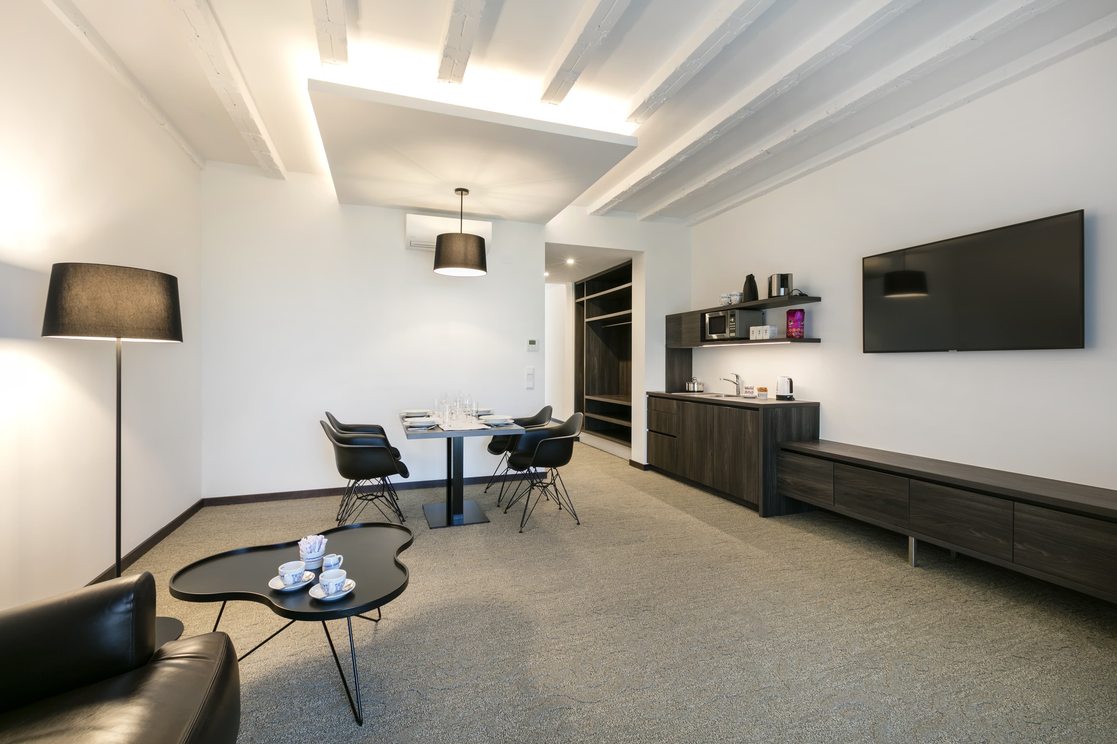 A stylish superior apartment at Hotel Spitzerberg by b_smart with modern interior, a dining table, black chairs, a kitchenette, and a TV on the wall.