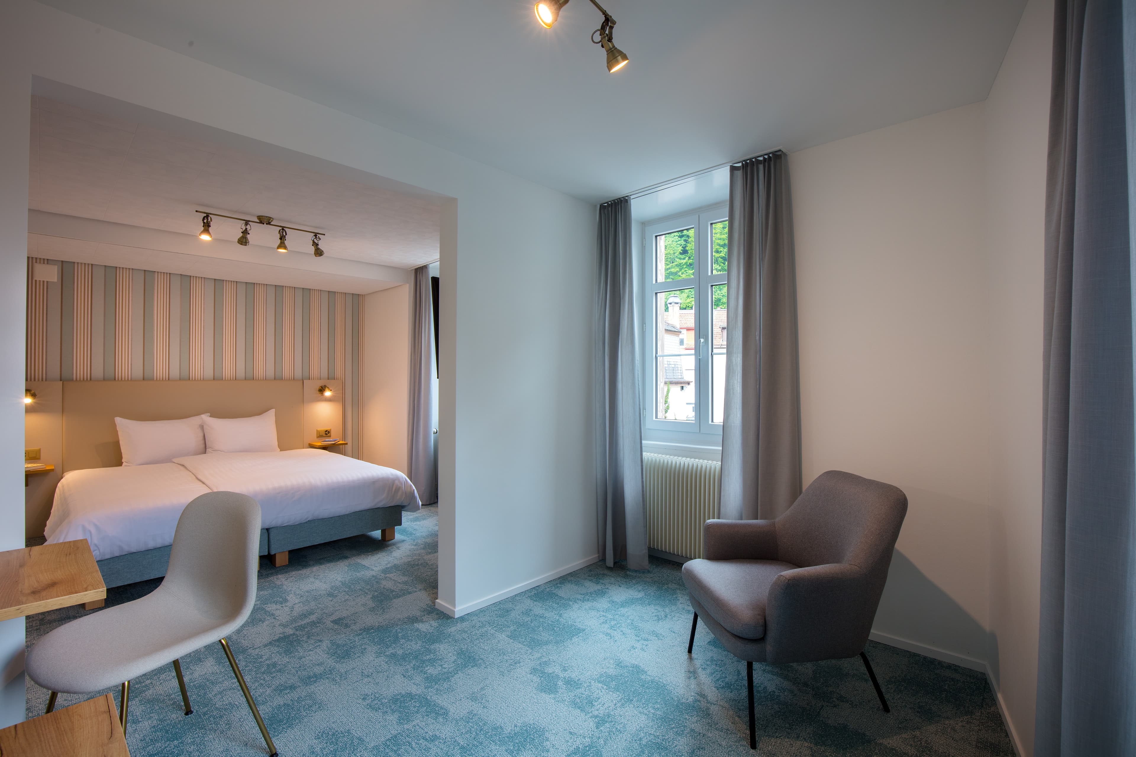 A modern hotel room in the Junior Suite at Hotel Krone with a large bed, sitting area, and bright windows.