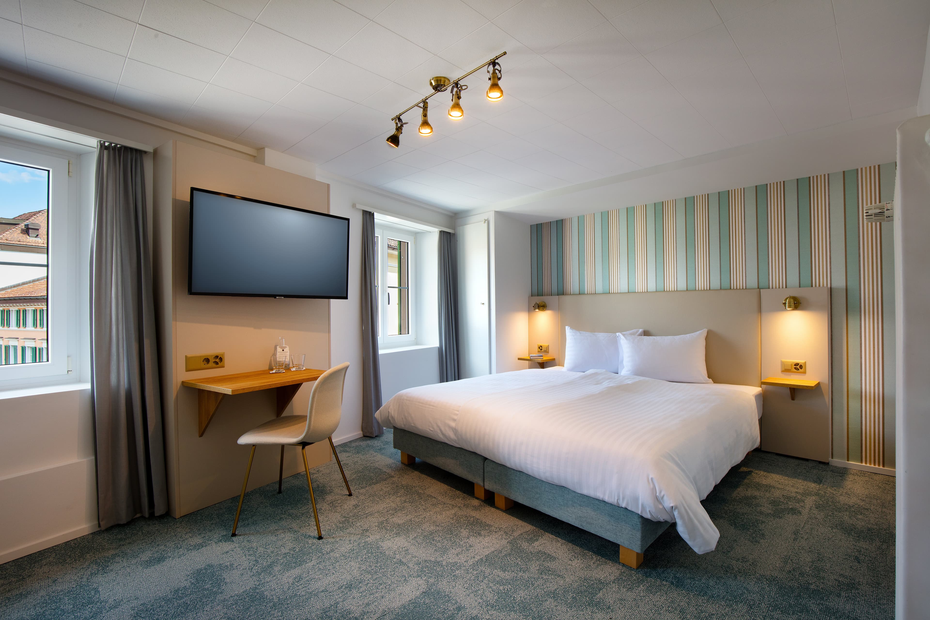 Bright and modern double room at Hotel Krone with a large bed, flat screen TV, two windows, and a small desk with a chair